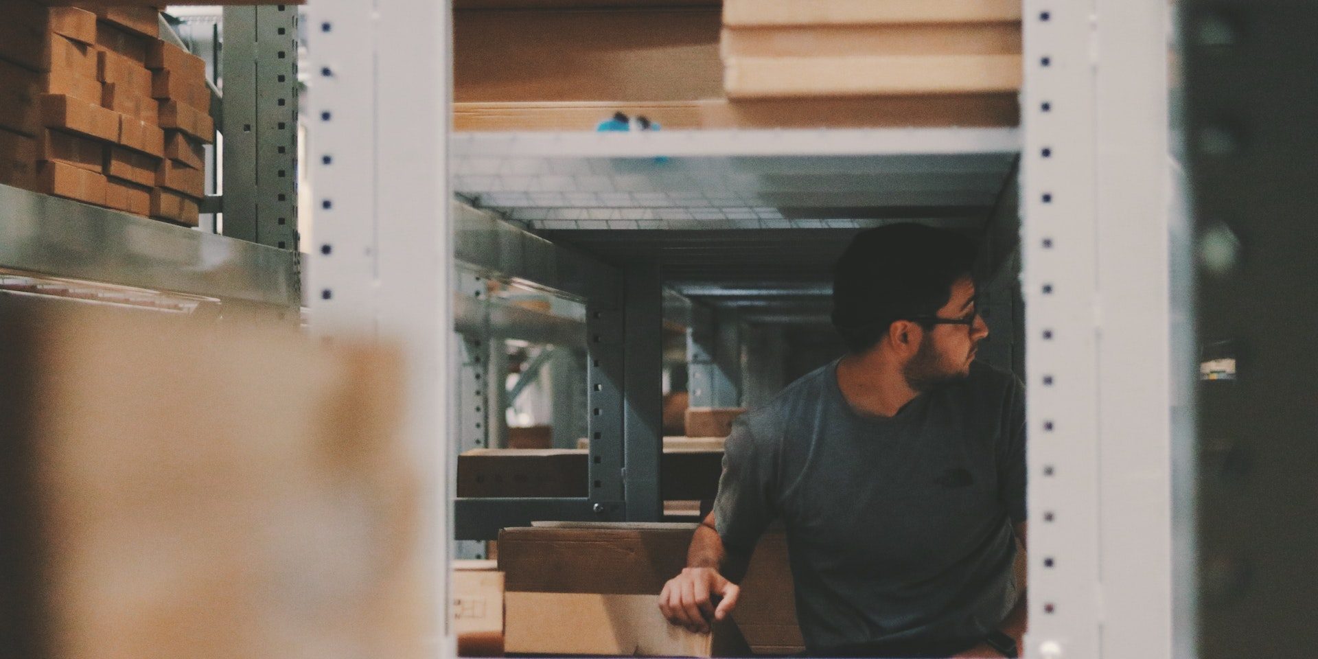 pexels-alexander-isreb-1797415 man handling boxes between warehouse shelving