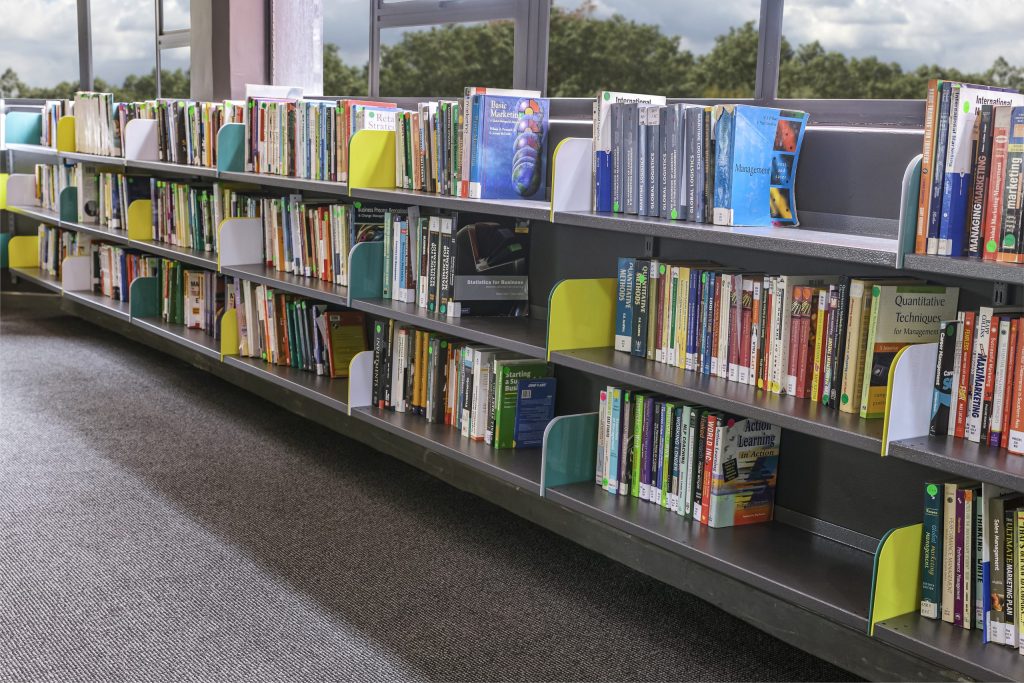 Library shelving lined with business and marketing books, under natural light from surrounding windows