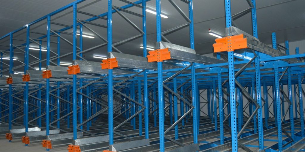 Interior of a warehouse featuring a pallet shuttle racking system vs rivet shelving with blue vertical frames and orange horizontal beams, demonstrating a high-density storage solution.