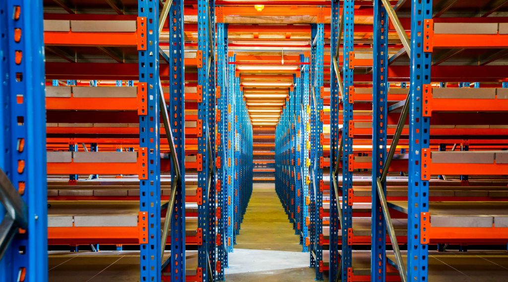 Interior view of an empty warehouse with tall orange and blue tightly stacked mezzanine floor metal shelving units