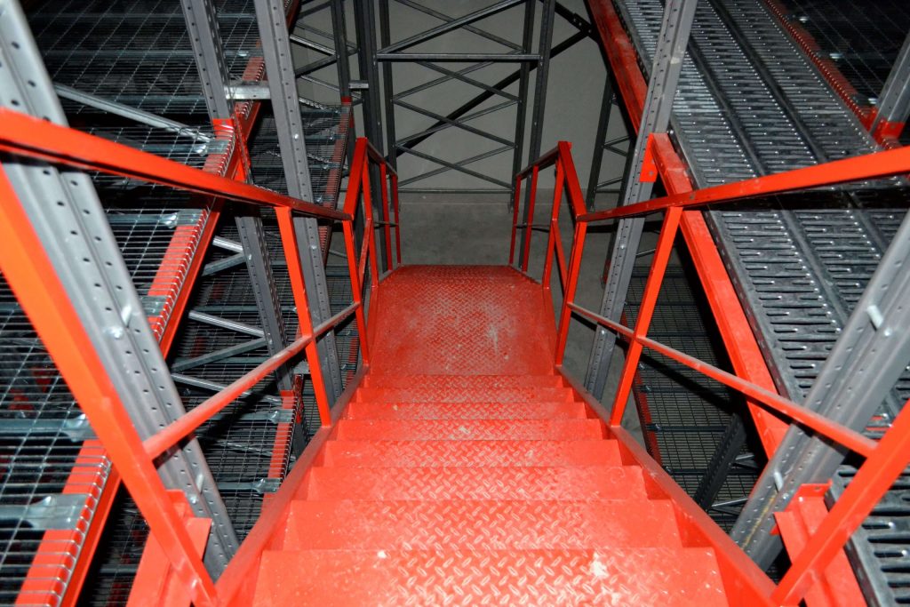 Catwalk racking vs. selective pallet racking. Newly built red catwalk racking system staircase in an empty warehouse.