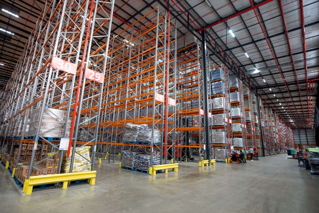 Large warehouse with tall selective pallet racking structures stacked with unitised pallets and staff members beside them