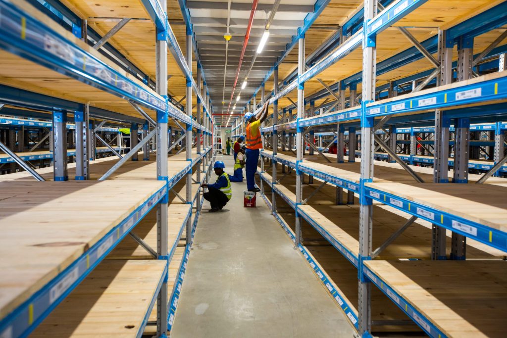 Workers installing pick face racking systems in a large warehouse.