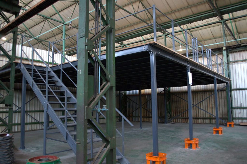 Grey structural mezzanine floor on orange stands in a large and empty warehouse