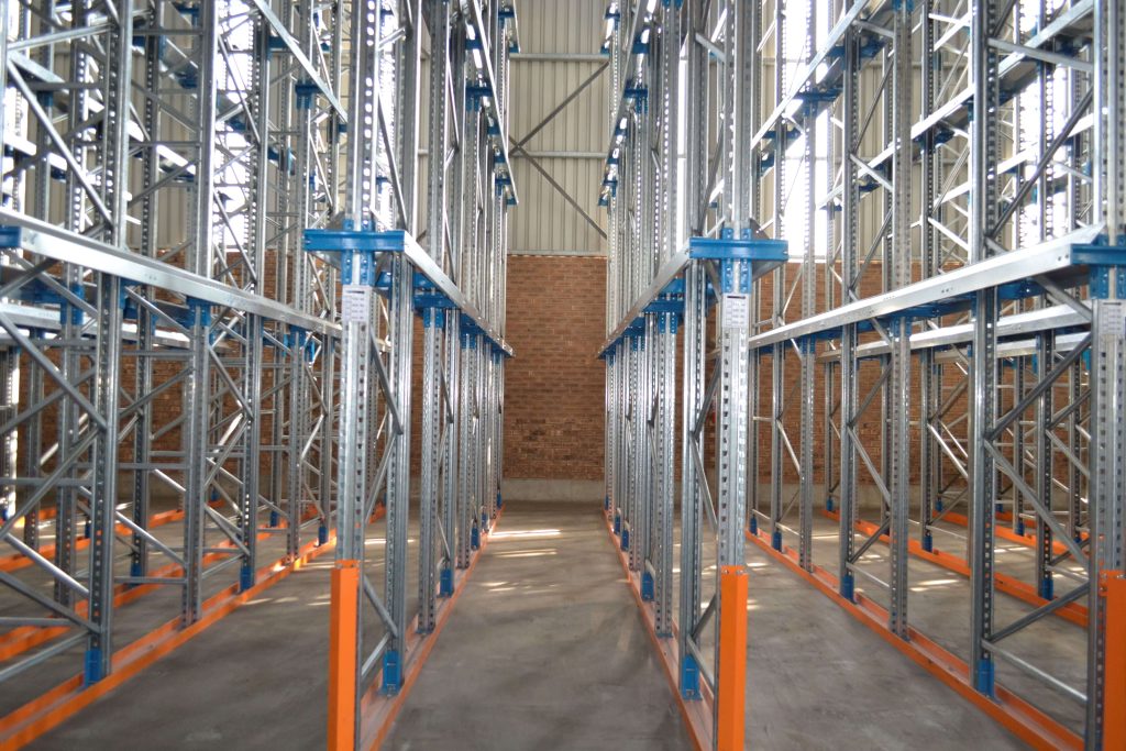 Tall metal drive-in racking structure with blue connectors and an orange base