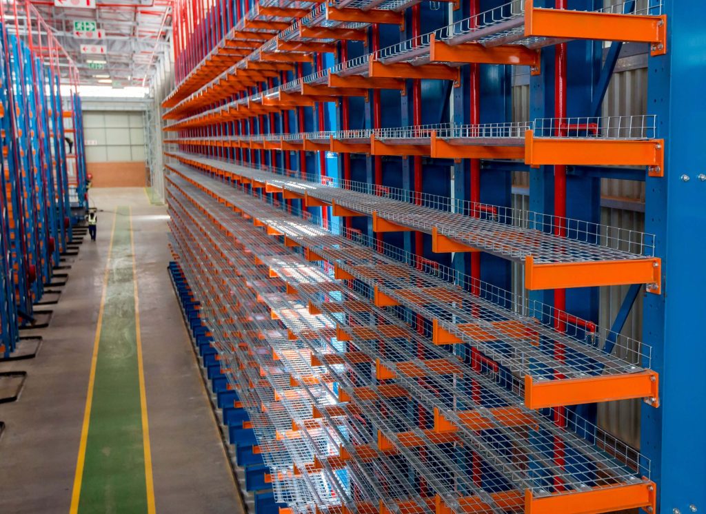 Large blue and orange cantilever racking in a warehouse with a worker walking in the aisle