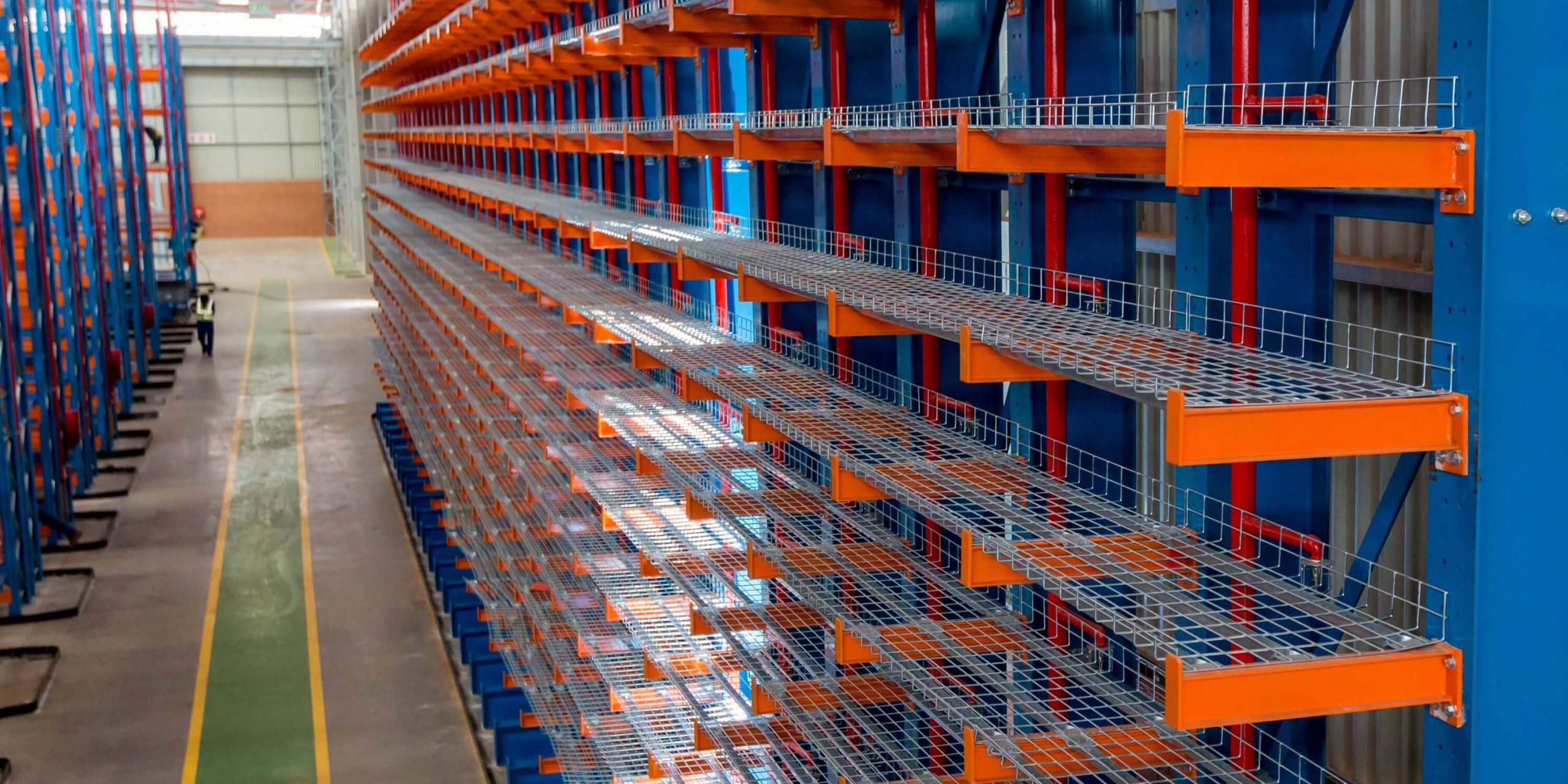 Krost-103 Large blue and orange cantilever racking in a warehouse with a worker walking in the aisle