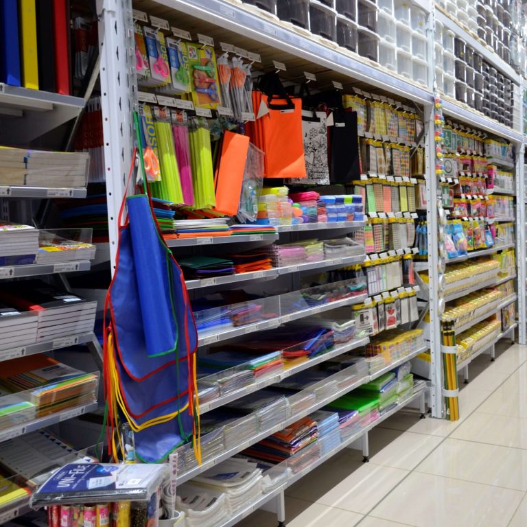 High gondola shelving neatly stacked with stationary and storage bins in a bright supermarket