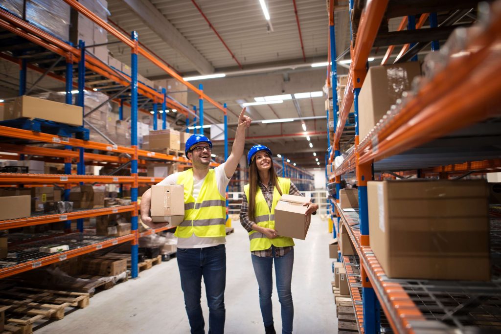 Man and woman standing in a warehouse racking aisle taking boxes from high shelves