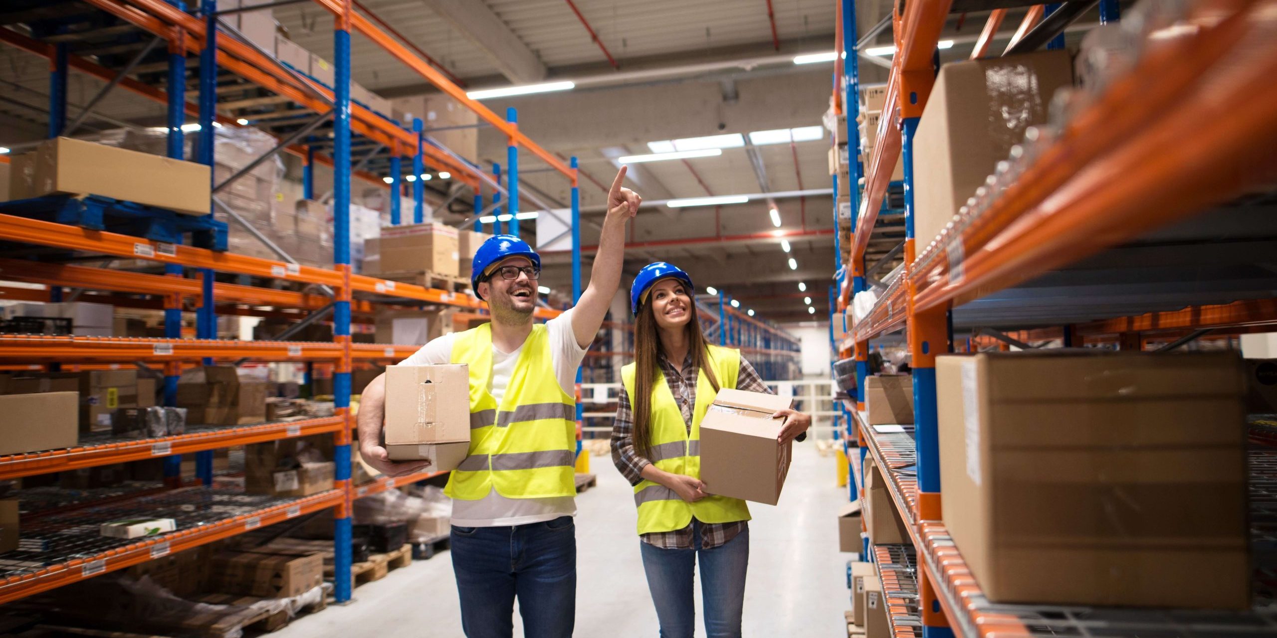 Man and woman standing in a warehouse racking aisle taking boxes from high shelves