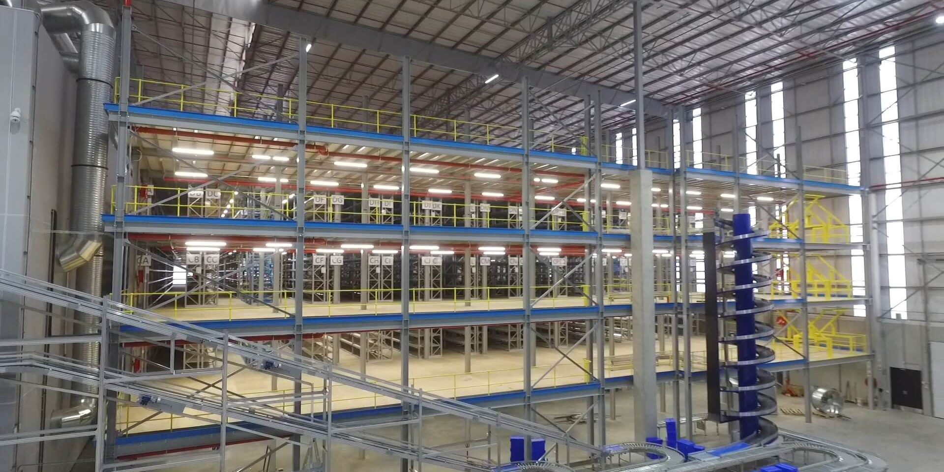 Krost_2 Structural mezzanine floors in a large industrial warehouse, featuring multiple levels of storage racks, safety railings, and integrated conveyor systems.