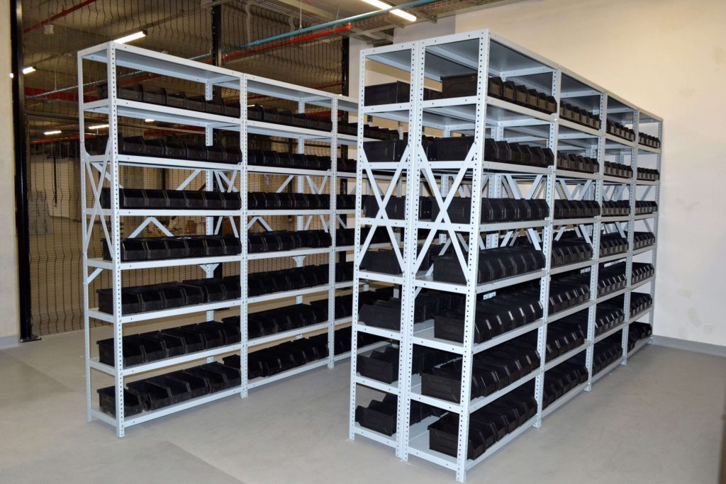 Bolted shelving stocked with empty black storage bins in a warehouse setting