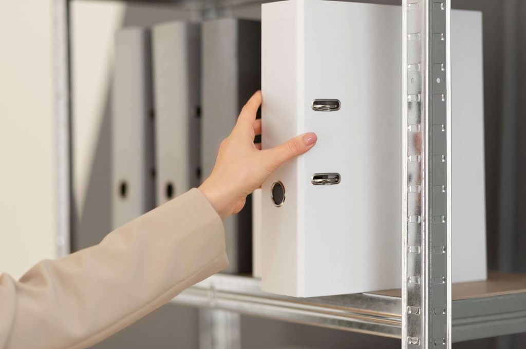 Young female office worker storing a file on an office shelving structure in a professional setting