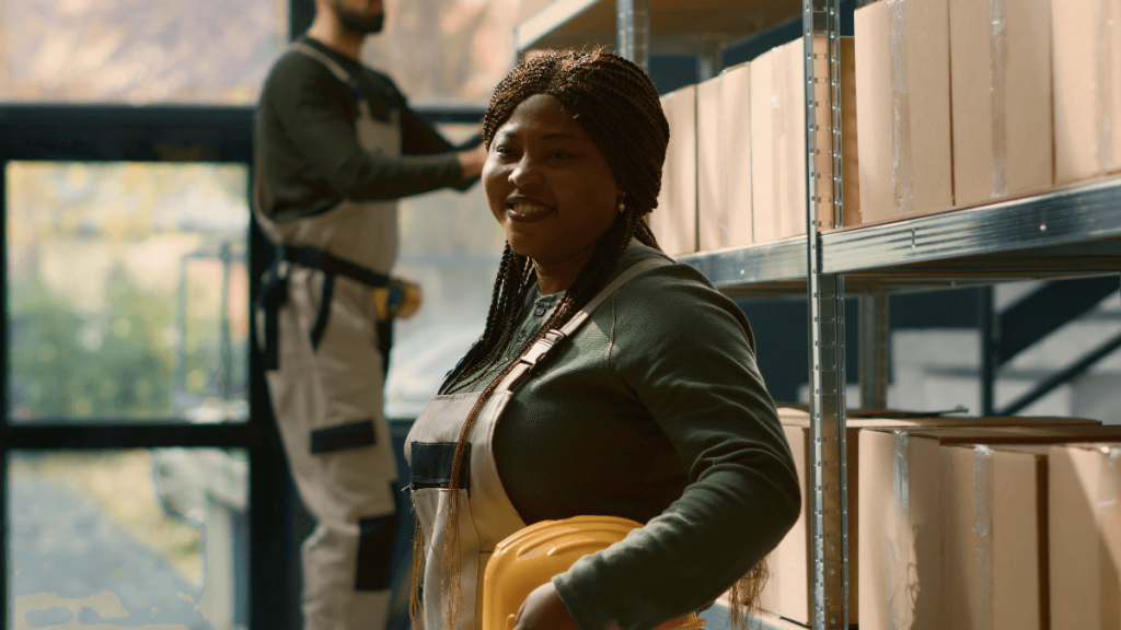 Factory vs. warehouse shelving: smiling female warehouse worker standing in front of stacked steel shelving