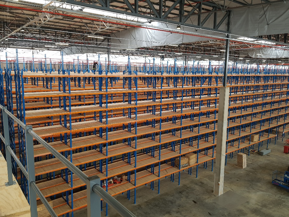 A worker standing on and installing a multilevel warehouse shelf