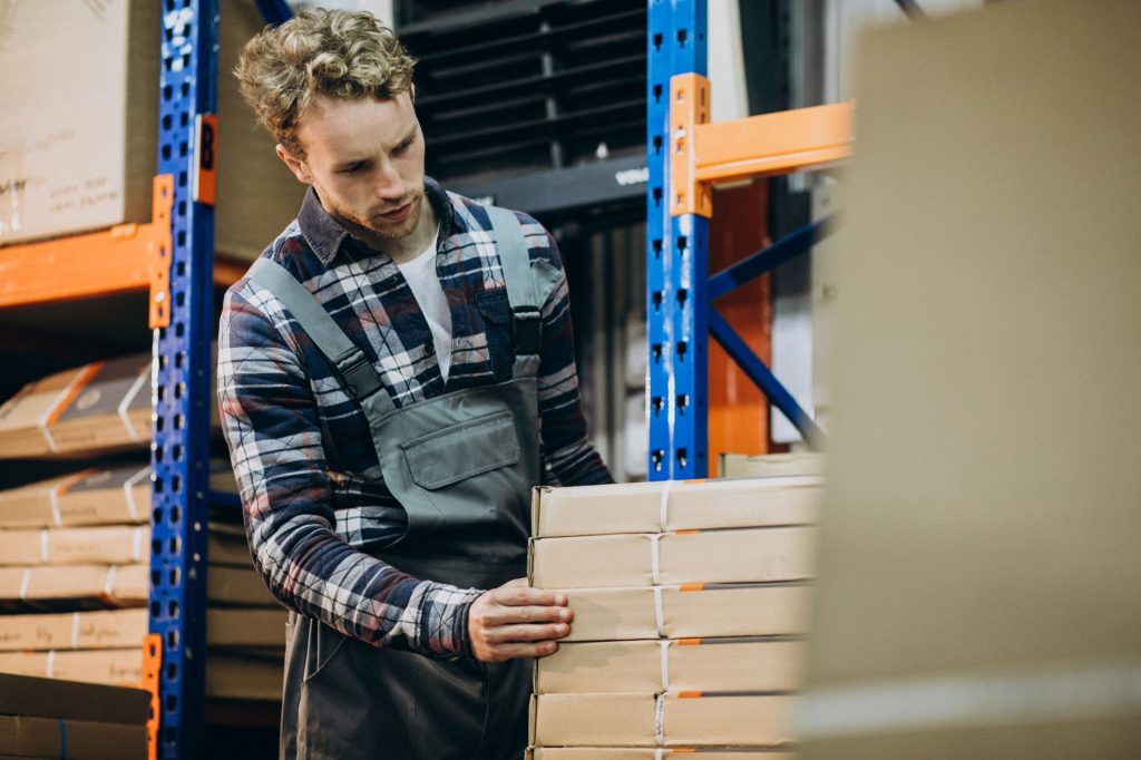 Pallet shuttle vs. structural mezzanine racking: male worker stacking boxes into warehouse shelves