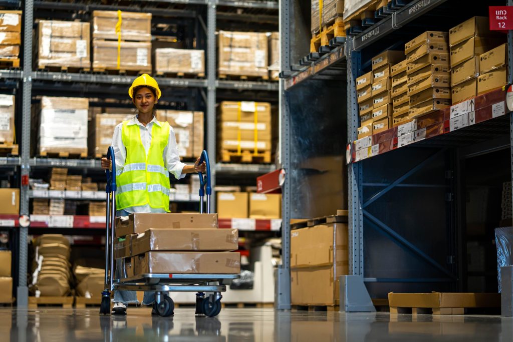 Distribution vs. fulfilment centre: smiling worker pushing boxes on a warehouse trolley