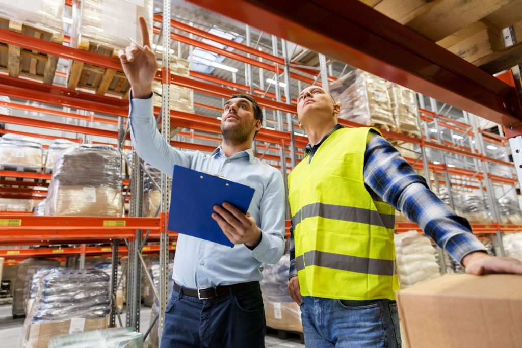 A worker and a businessman with a clipboard at a warehouse examining drive-through vs. pallet-shuttle racking