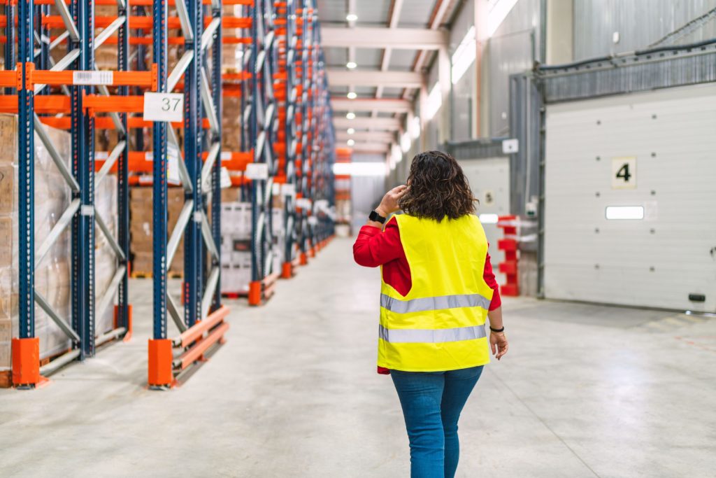Female supervisor walking through logistics warehouse and using smartphone