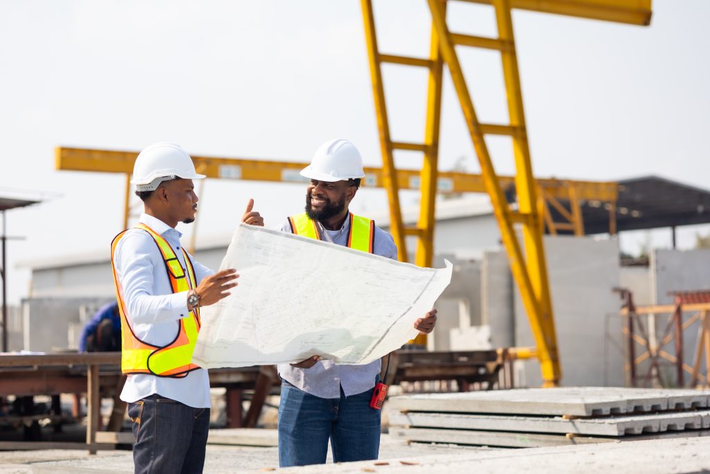 An engineering team standing with a plan, discussing construction warehouse shelving on site