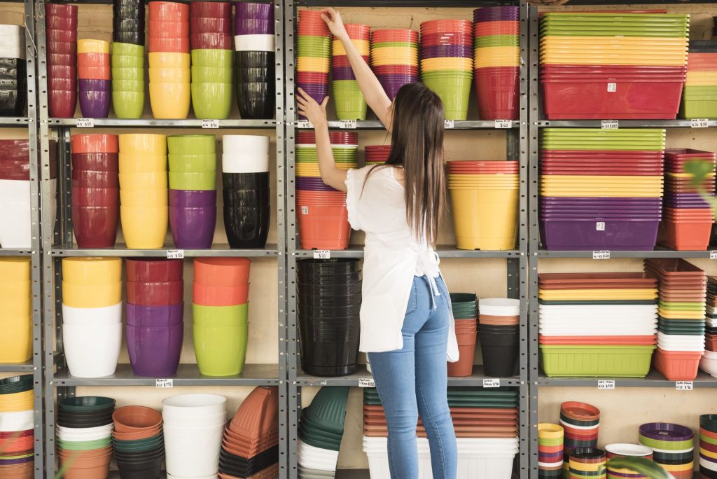 Rivet shelving vs. structural mezzanines: A young woman picking flower pots from a set of rivet shelves