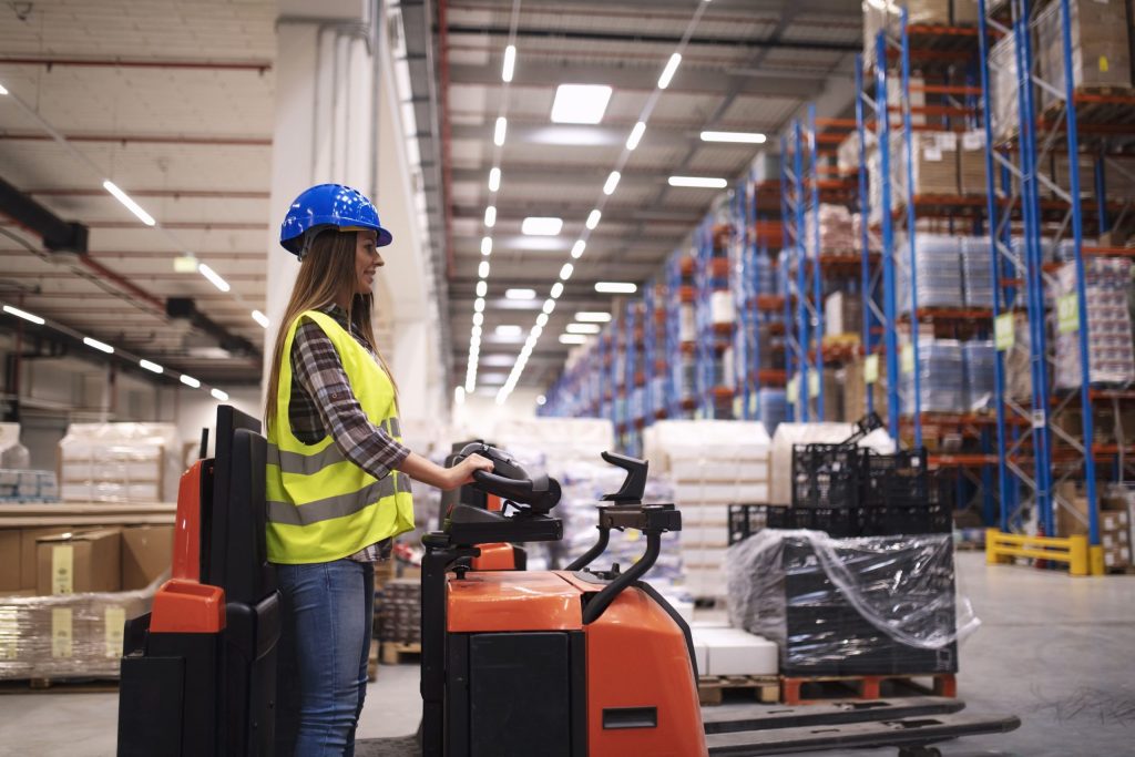 Ajustable vs. VNA pallet racking: A female worker in a large warehouse operating a forklift