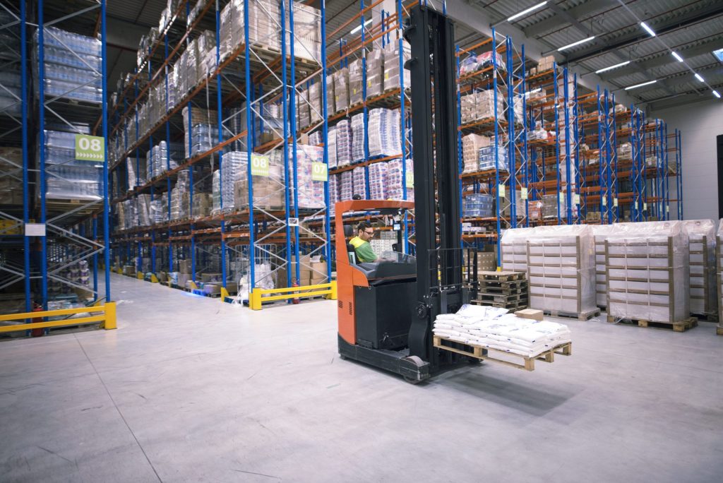 Adjustable vs. mobile pallet racking: A worker using a forklift in a large warehouse filled with stacked pallet racks