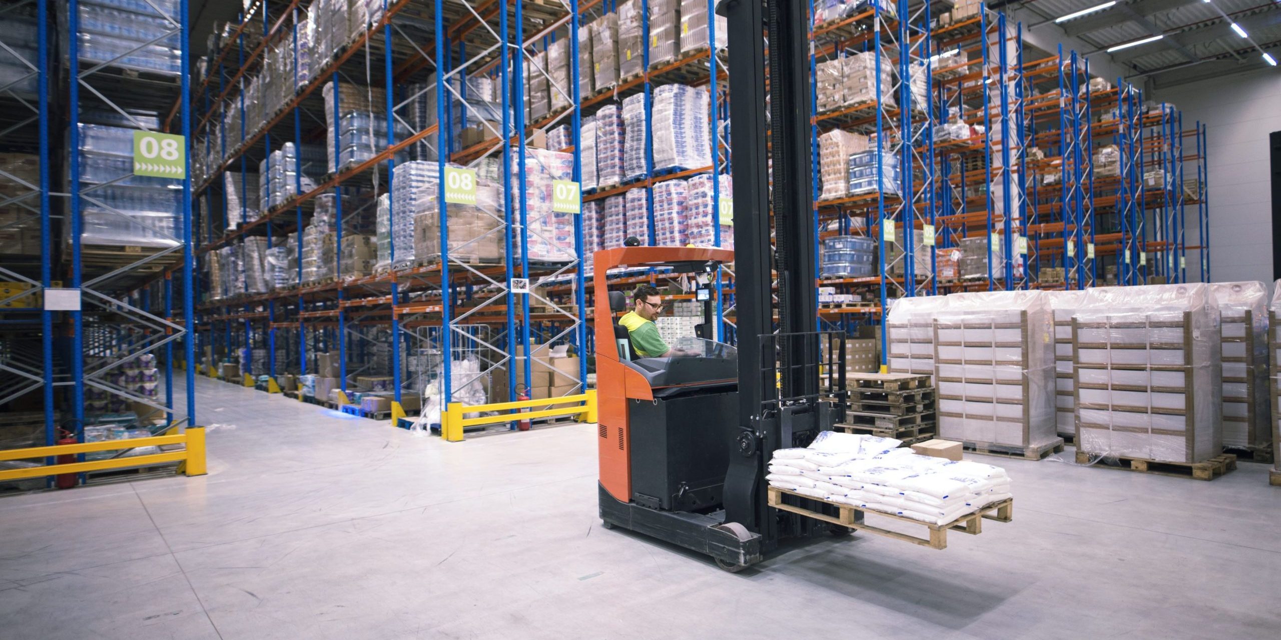Adjustable vs. mobile pallet racking: A worker using a forklift in a large warehouse filled with stacked pallet racks