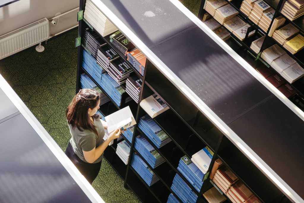 A person browsing bookshelves in a library or office space, organizing materials on industrial shelving units.