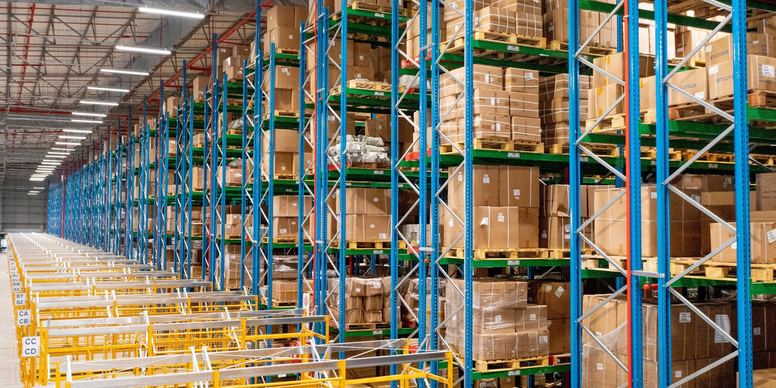 A large, densely stacked VNA rack in a warehouse showing how rivet shelving and VNA racking compare. A large, densely stacked VNA rack in a warehouse showing how rivet shelving and VNA racking compare.