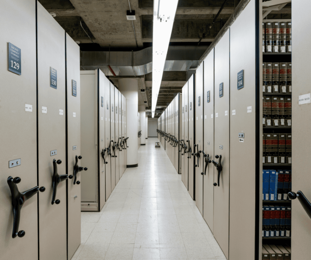 A long row of mobile shelving in a school storeroom that’s stacked with books