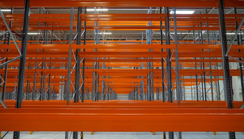 Empty warehouse racking with orange steel beams, comparing modular vs fixed shelving systems for scalable storage.