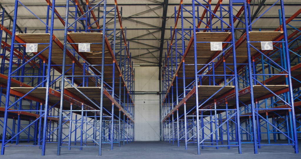 Empty warehouse with tall blue and orange industrial shelving arranged in numbered aisles for pallet storage and logistics.
