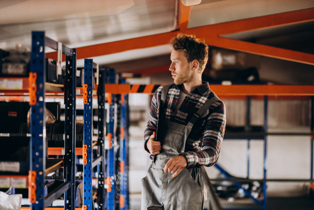 Technician walking through industrial shelving in a warehouse while checking stock and equipment.